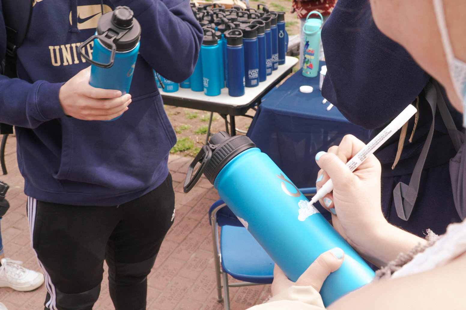 Person holding a blue water bottle in their hand draws a white cloud on the surface with paint pen.
